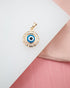 A gold evil eye pendant rests on a white and pink display surface.