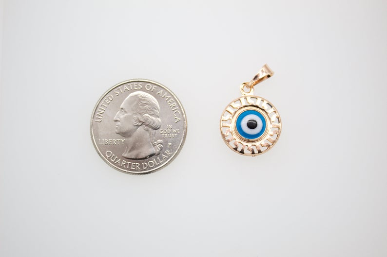 A gold Greek key evil eye pendant rests next to a US quarter coin for scale.