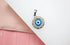 A silver evil eye pendant rests on a white and pink background.