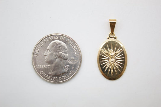 A gold crucifix pendant rests next to a US quarter coin to show its size.
