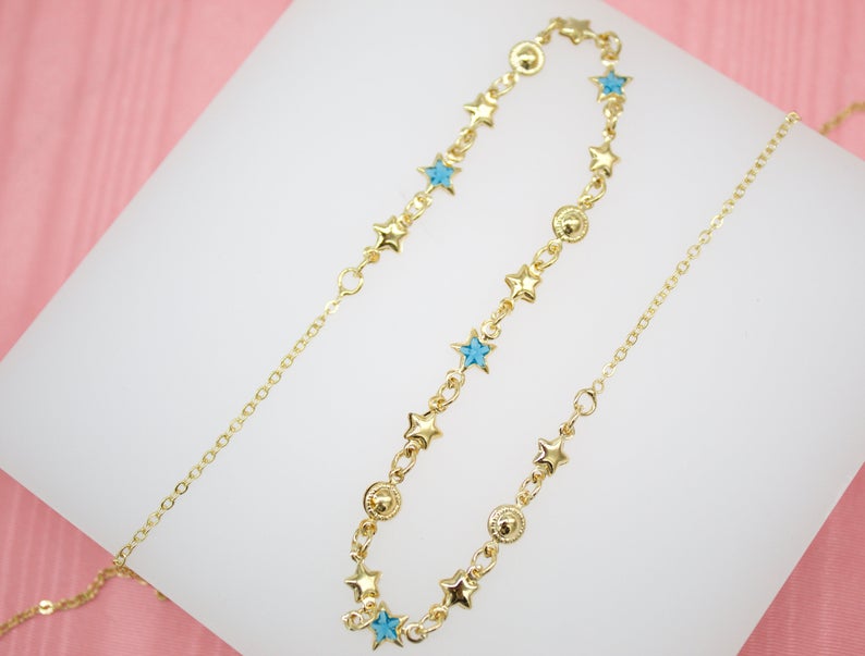 A delicate gold chain necklace sparkles with alternating blue star charms and metallic beads against a white display surface.