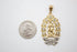 A gold Our Lady of Guadalupe pendant rests next to a US quarter coin for size comparison on a white surface.