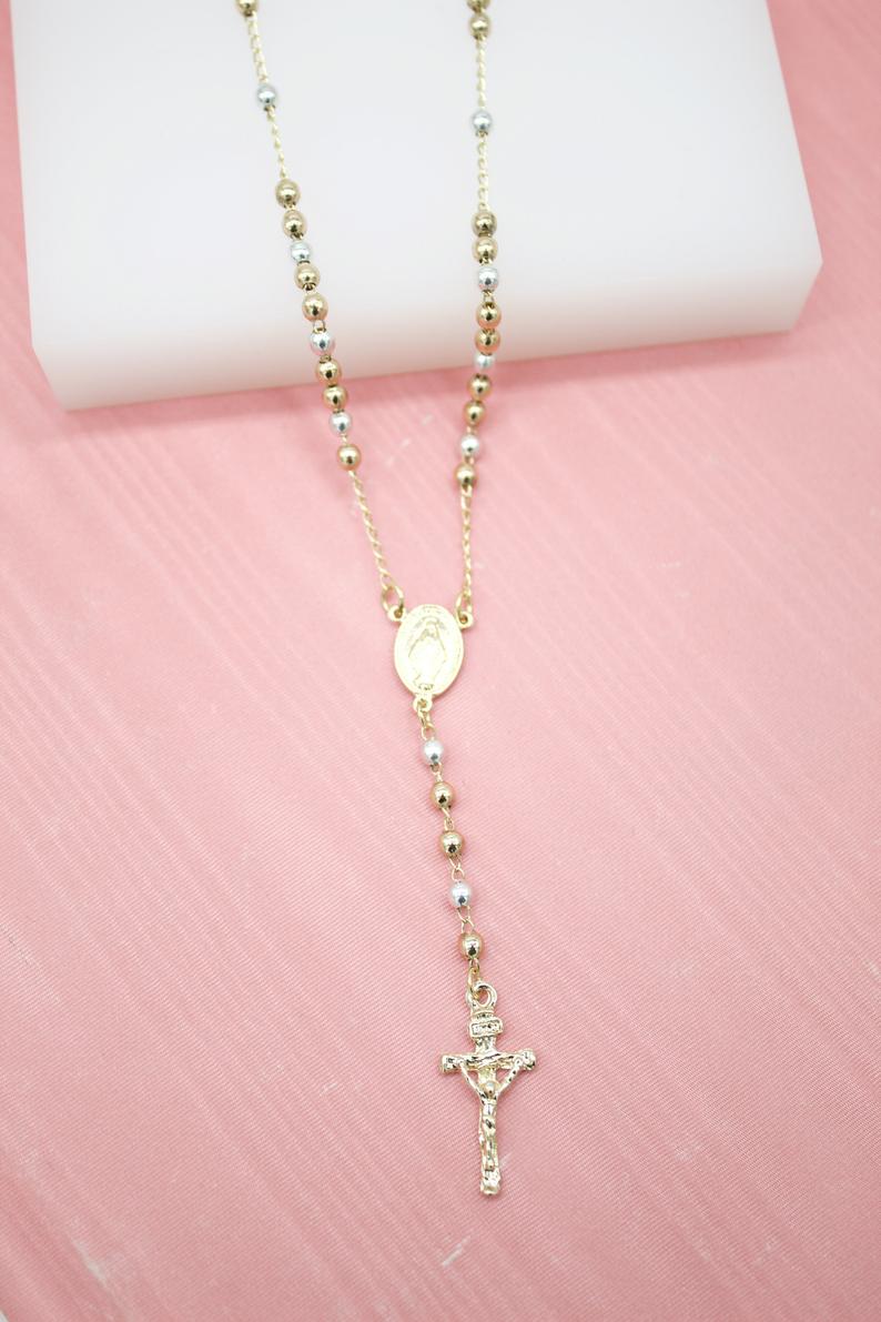 A gold and silver rosary necklace rests gracefully on a pink surface.