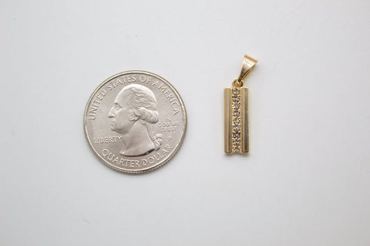 A gold rectangular pendant featuring a vertical row of sparkling cubic zirconia stones rests next to a US quarter coin for size comparison on a white surface.