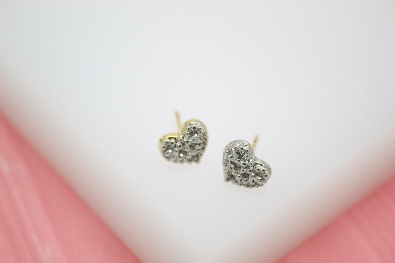 A pair of sparkling pavé diamond heart stud earrings rests on a white display surface.