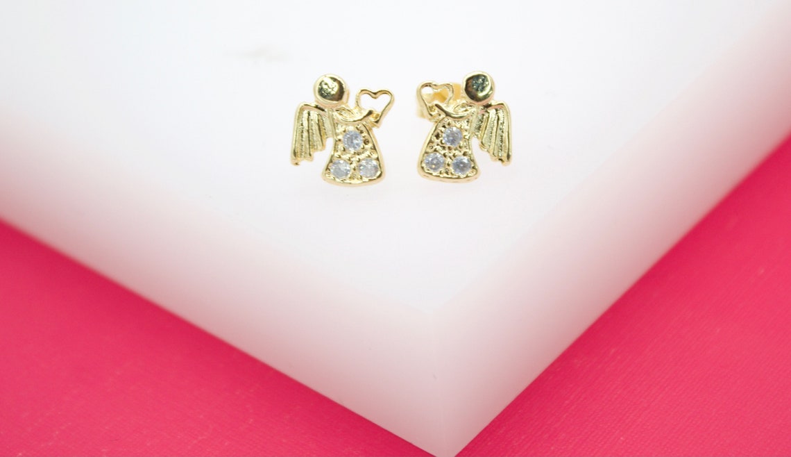 A pair of gold angel stud earrings featuring sparkling cubic zirconia stones rest on a white display stand.