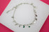 A delicate silver charm bracelet featuring dangling stars, moons, and hearts lies displayed on a white surface.