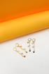 A pair of gold and a pair of silver star-dangle hoop earrings rest on a white surface against an orange backdrop.