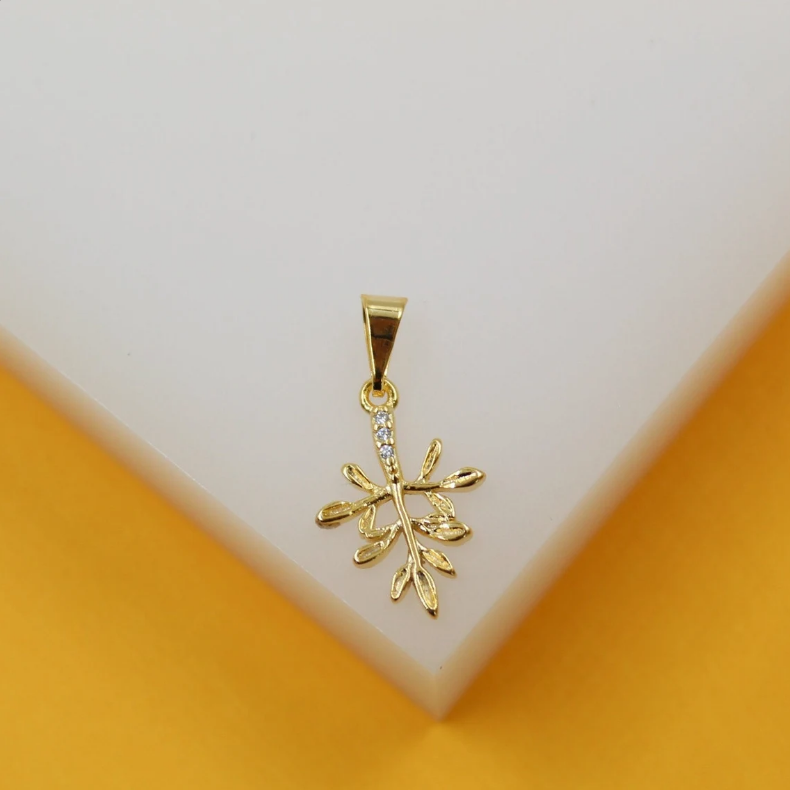 A delicate gold pendant shaped like a leafy twig, accented with small cubic zirconia stones, rests against a white and yellow display surface.