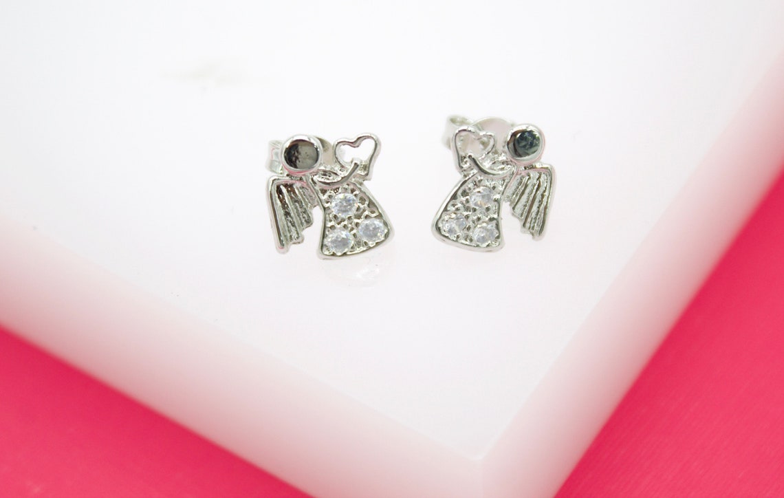 A pair of silver angel earrings with sparkling cubic zirconia stones rests on a white display surface.