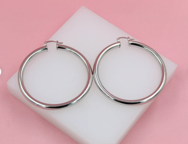 A pair of polished silver hoop earrings rests on a white display block against a pink background.