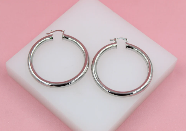 A pair of polished silver hoop earrings rests on a white display block against a pink background.