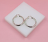 A pair of polished silver hoop earrings rests on a white block against a soft pink background.