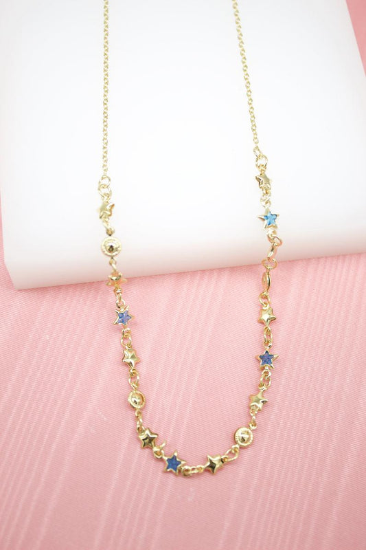 A delicate gold star pendant necklace rests against a soft pink backdrop, featuring scattered blue enamel star charms along its chain.