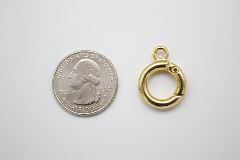 A gold spring ring clasp rests beside a US quarter for scale on a white surface.