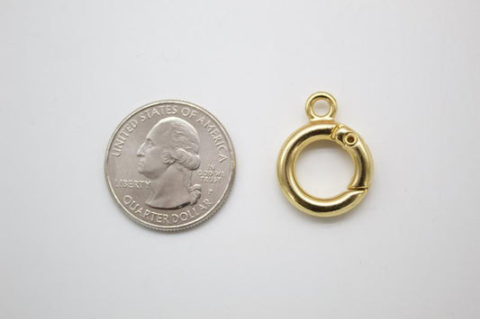 A gold spring ring clasp rests beside a US quarter for scale on a white surface.