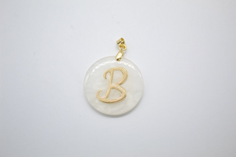 A round white pendant features an ornate gold initial B in the center.