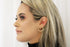 A blonde woman wearing a stylish gold chain-link hoop earring gazes thoughtfully in profile.