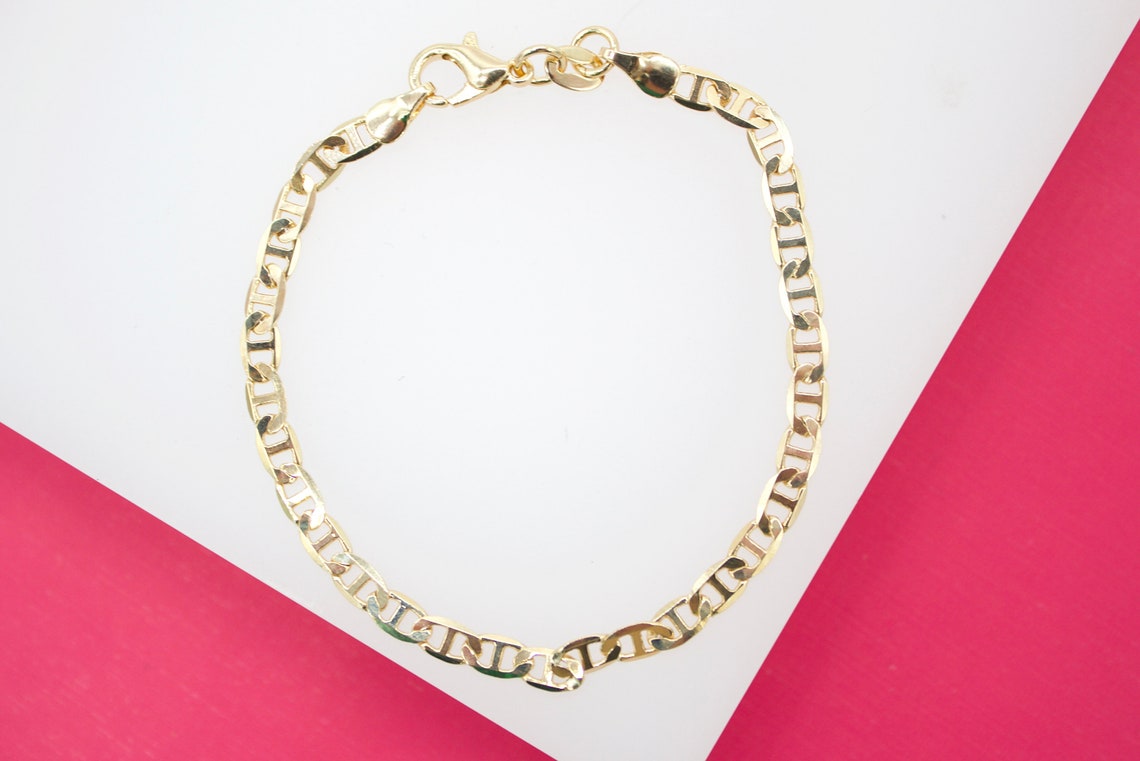 A shiny gold mariner link bracelet rests flat on a white and pink display surface.