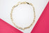 A shiny gold mariner link bracelet rests flat on a white and pink display surface.