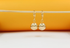 A pair of shiny gold ball drop earrings hangs delicately from a thin stick against a warm orange background.