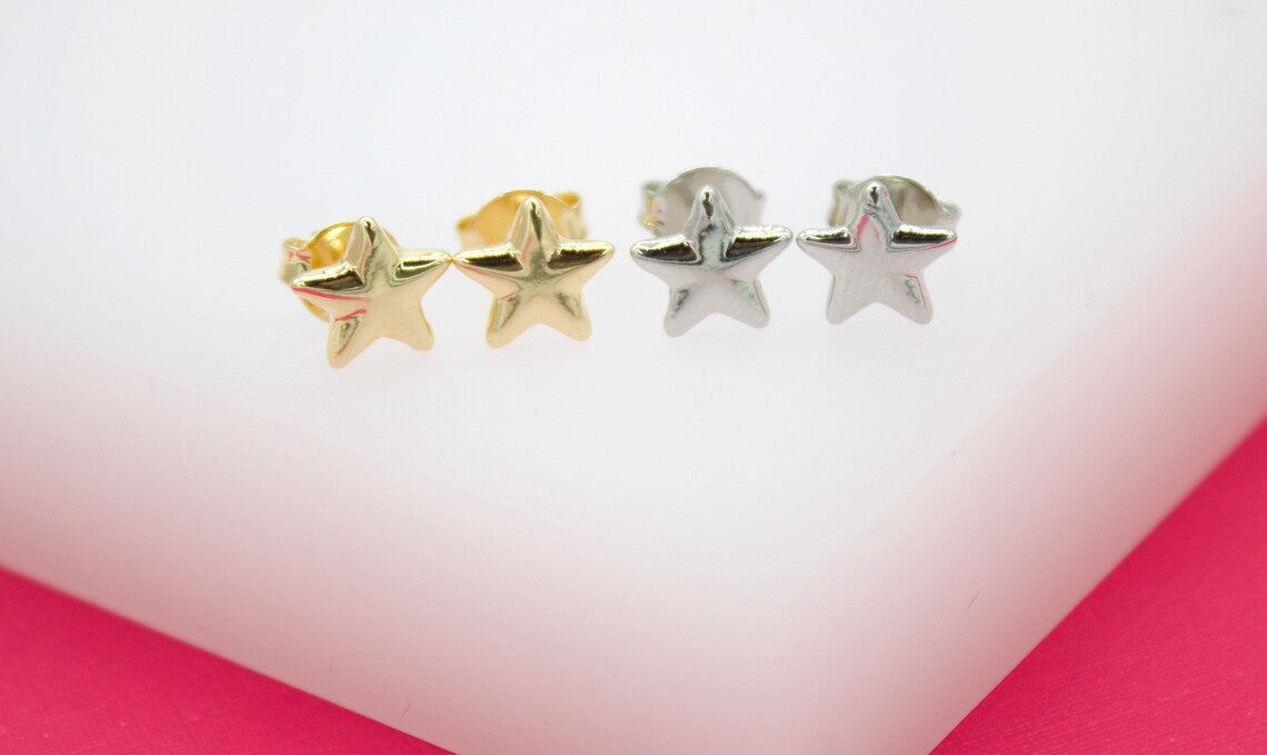 Four polished star-shaped stud earrings in gold and silver finishes rest side by side on a white surface.