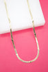 A flat gold herringbone chain necklace adorned with small heart charms rests against a white display block and vibrant pink background.