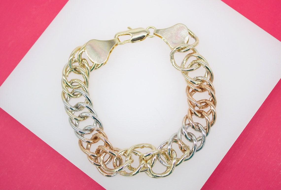 A tri-color gold chain link bracelet rests on a white and pink surface.