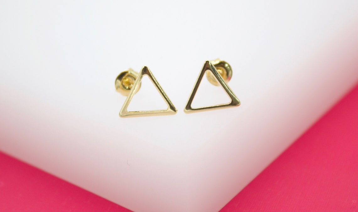 A pair of minimalist gold triangle stud earrings rests neatly on a white and pink display surface.