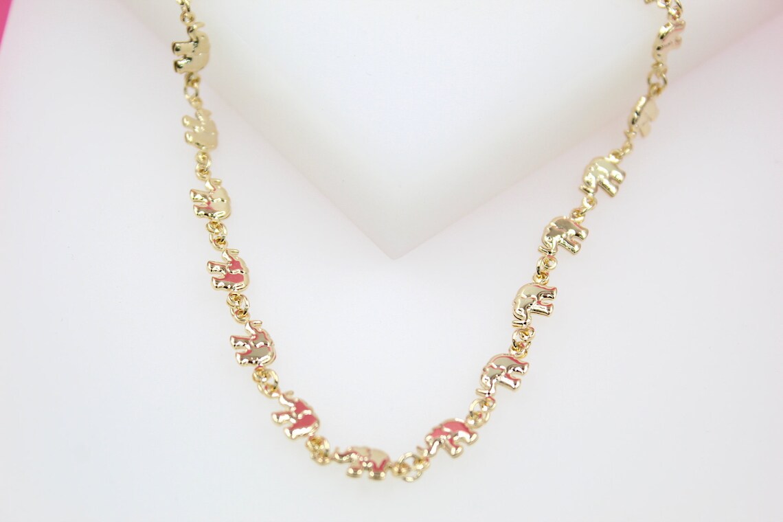 A gold necklace featuring a delicate chain of linked elephant charms rests against a white display surface.