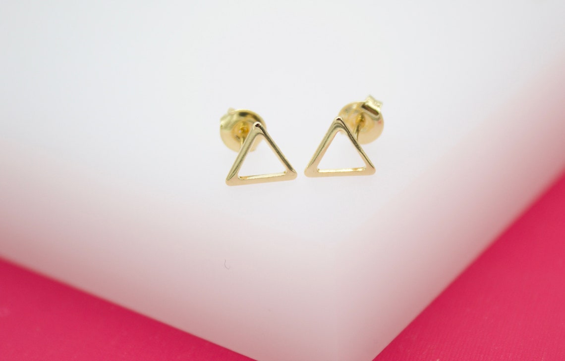 A pair of minimalist gold triangle stud earrings rests neatly on a white display surface.