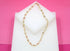 A gold elephant charm necklace is displayed on a white display block against a vibrant pink background.