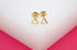 A pair of minimalist gold triangle stud earrings rests neatly on a white display block against a vibrant pink background.