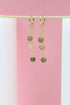 A pair of elegant gold chain dangle earrings with small circular charms hangs gracefully against a minimalist pink and white backdrop.