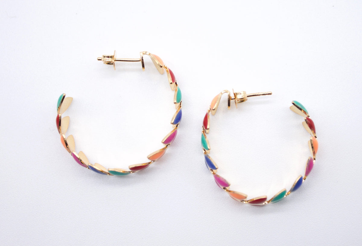 A pair of gold hoop earrings embellished with colorful enamel sections rest on a white surface.