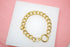 A thick gold chain bracelet rests on a white display surface against a pink background.