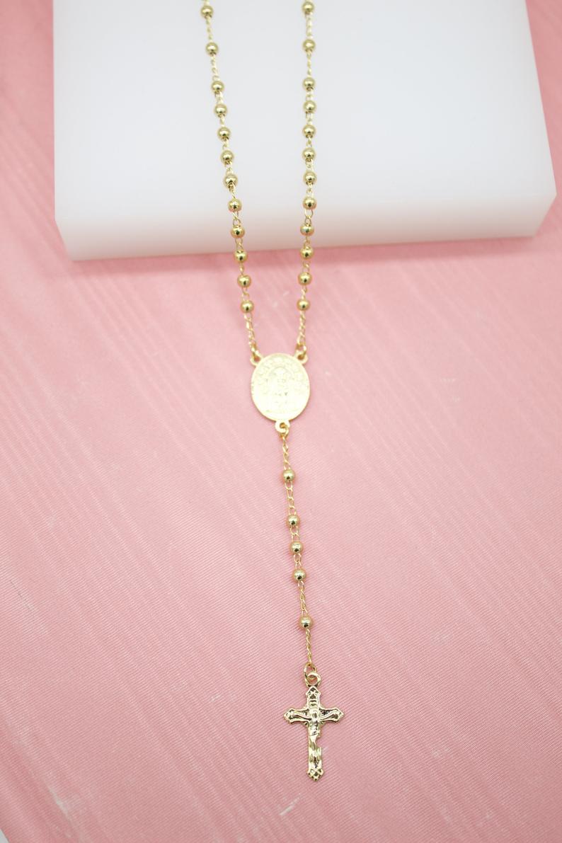 A delicate gold rosary necklace rests against a soft pink background, featuring shiny beaded links and a detailed crucifix pendant.