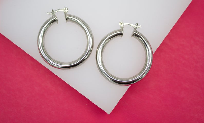 A pair of polished silver hoop earrings rests on a white display against a vibrant pink background.