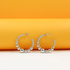 A pair of silver ball hoop earrings rests on a white surface against a bright orange background.