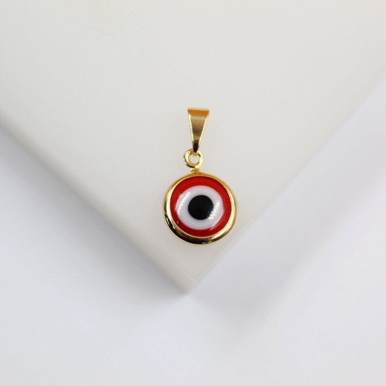 A gold-framed pendant featuring a red, white, and black evil eye design rests on a white surface.