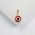 A gold-framed pendant featuring a red, white, and black evil eye design rests on a white surface.