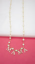 A delicate gold pearl necklace features rhinestone-encrusted letters spelling out "MAMA" against a pink background.
