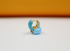 A pair of vibrant light blue enameled gold hoop earrings sits prominently on a white surface against an orange backdrop.