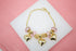 A gold charm bracelet featuring pink crystal beads and dangling heart charms rests on a white display surface.