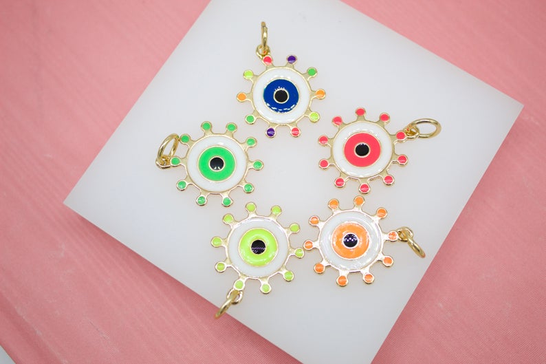 Five colorful enamel evil eye charms with gold sunburst borders rest on a white display surface.