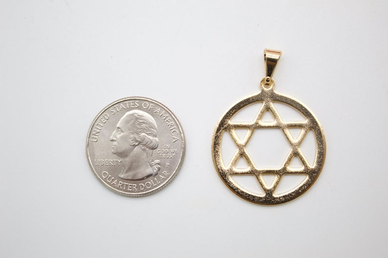 A gold Star of David pendant rests beside a US quarter for size comparison on a white surface.