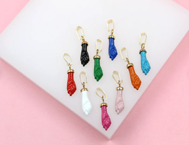 A colorful collection of figa hand pendants in various enamel colors rests on a white display surface.