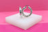 A pair of chunky silver twist hoop earrings rest on a white display block against a vibrant pink backdrop.
