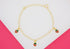 A gold chain bracelet features three hanging enamel strawberry charms against a pink and white background.