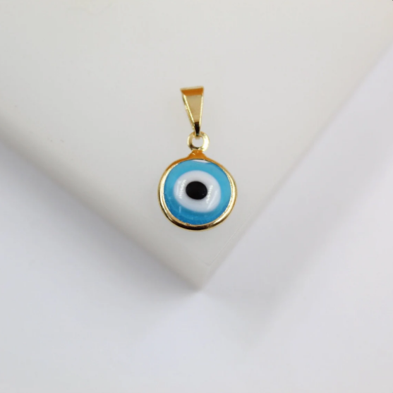 A round gold-framed evil eye pendant rests on a white surface, showcasing concentric circles of blue, white, and black enamel.